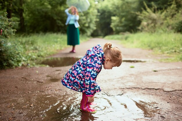La giovane mamma e la piccola figlia si divertono camminando negli stivali di gomma sulle piscine in parco