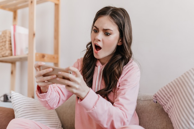 La giovane modella dai capelli scuri si siede nella sua stanza e prende selfie con l'espressione facciale sorpresa