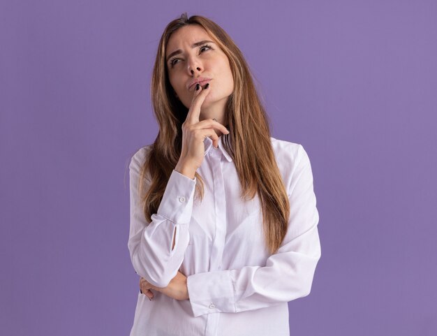 La giovane ragazza abbastanza caucasica premurosa mette la mano sul mento e alza lo sguardo sulla porpora