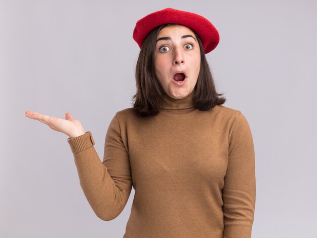 La giovane ragazza abbastanza caucasica sorpresa con il cappello del berretto tiene la mano aperta