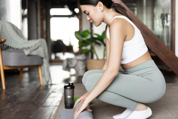 La giovane ragazza asiatica prepara il tappetino per la meditazione yoga o l'allenamento fitness a casa per l'allenamento a casa sua.