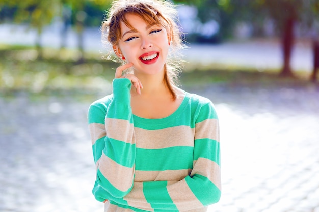 La giovane ragazza asiatica teenager abbastanza allegra che posa al parco della città in una bella giornata estiva, ha un umore giocoso positivo, sorride e si diverte, indossa un maglione a righe casual. Ritratto di stile di vita luminoso.
