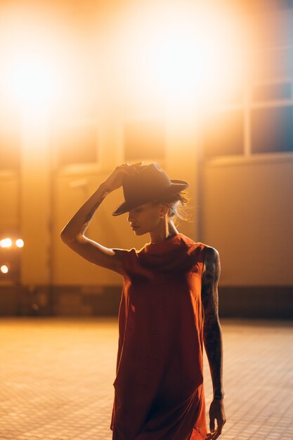 La giovane ragazza attraente in un cappello pone alla telecamera di notte