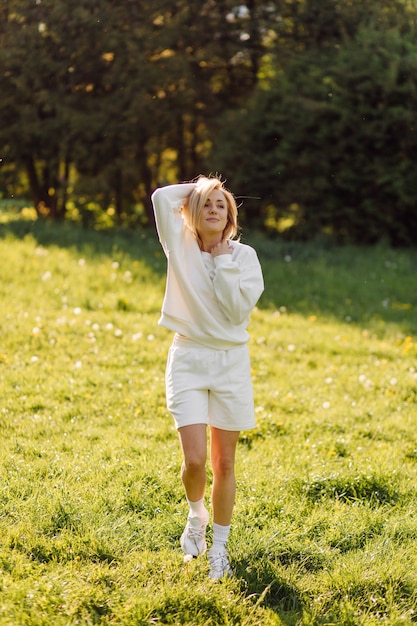 La giovane ragazza bionda indossa una felpa con cappuccio bianca sorridente e cammina nel bosco