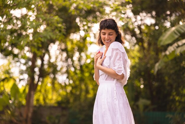 La giovane ragazza castana caucasica sveglia indossa un vestito bianco chiudendo gli occhi e si diverte a passare il tempo nella natura