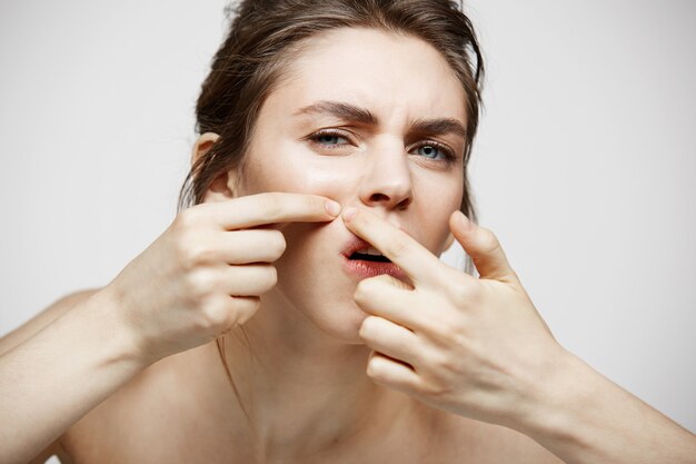 La giovane ragazza castana ha dispiaciuto della sua pelle del fronte dell'acne di problema sopra fondo bianco. Cosmetologia della salute e cura della pelle.