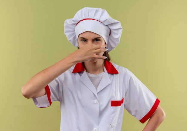 La giovane ragazza caucasica infastidita del cuoco in uniforme del cuoco unico chiude il naso con la mano sul verde con lo spazio della copia