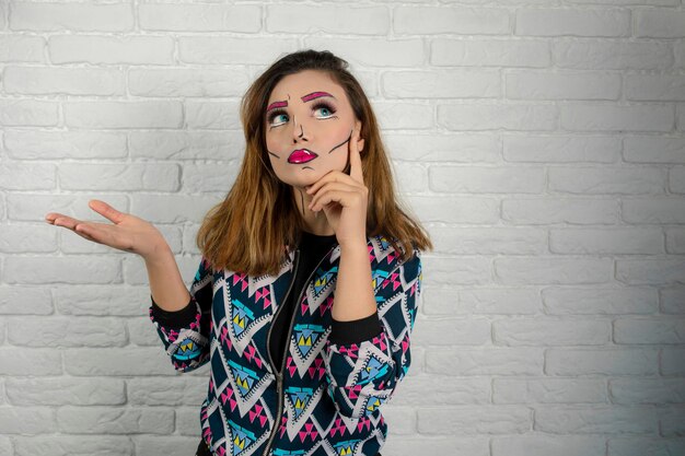 La giovane ragazza che indossa la fantasia si trucca e si mette la mano sul mento. Foto di alta qualità