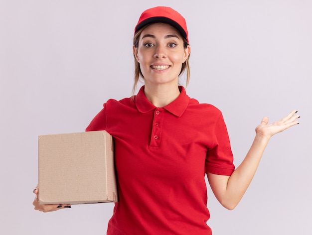 La giovane ragazza graziosa sorridente di consegna in uniforme tiene la mano aperta e tiene il cardbox su bianco