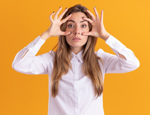 La giovane ragazza piuttosto caucasica scioccata apre gli occhi con le mani e guarda la telecamera