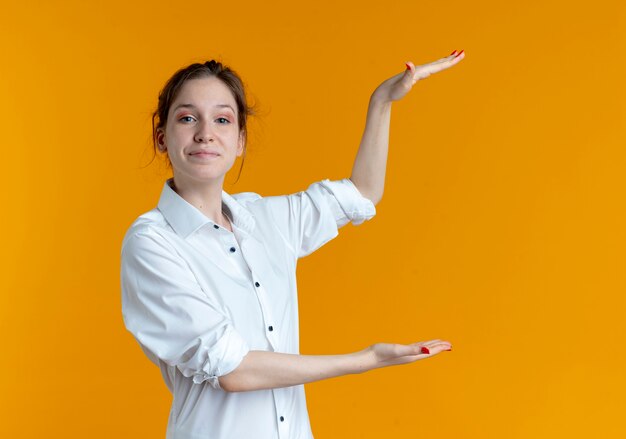 La giovane ragazza russa bionda felice finge di tenere qualcosa di isolato sullo spazio arancione con lo spazio della copia