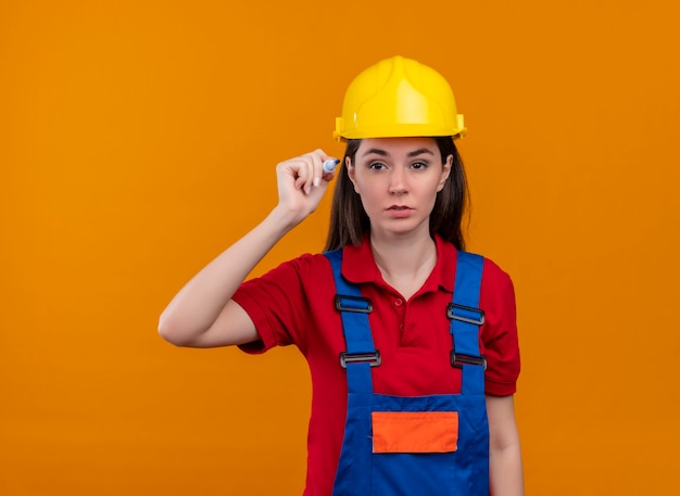 La giovane ragazza sicura del costruttore tiene il contrassegno su su fondo arancio isolato con lo spazio della copia