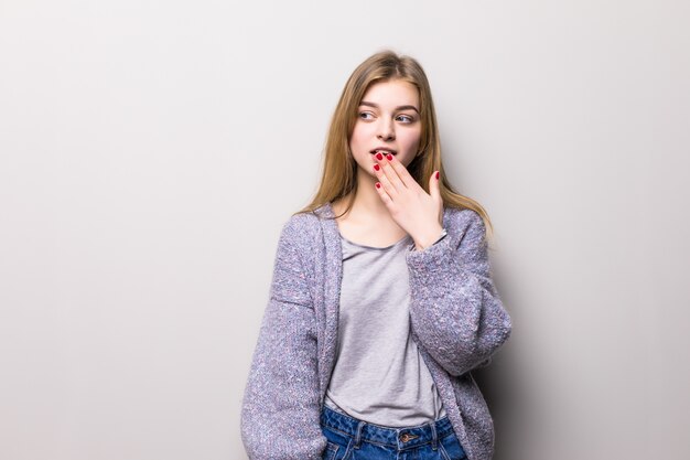 La giovane ragazza teenager copre la sua bocca nella mano di scossa su un muro grigio