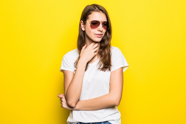 La giovane signora di pensiero in maglietta bianca e jeans blu rimane davanti al fondo giallo dello studio