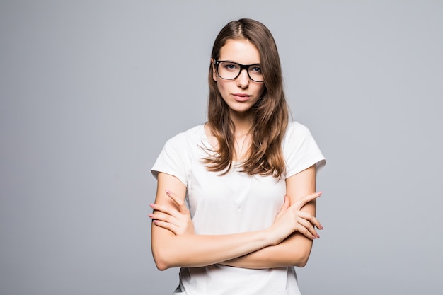 La giovane signora di pensiero serio in vetri in maglietta bianca e blue jeans rimane davanti al fondo bianco dello studio