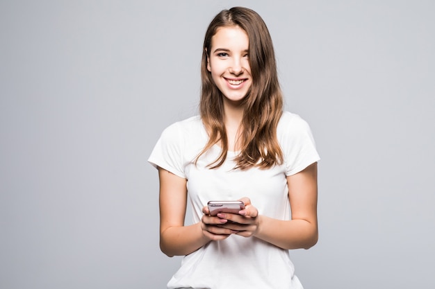 La giovane signora felice in maglietta bianca e blue jeans resta con il telefono davanti al fondo bianco dello studio