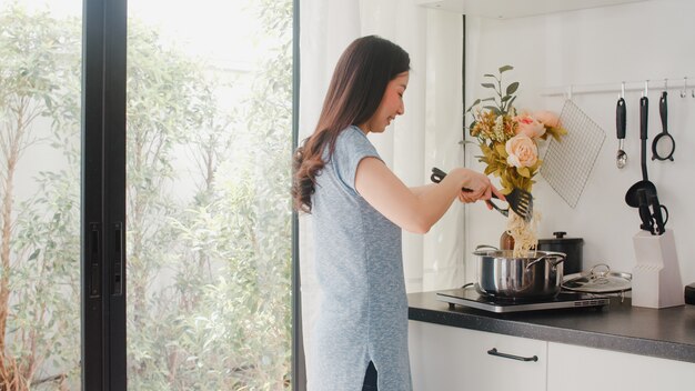 La giovane signora giapponese asiatica gode di cucinare a casa. Donne di stile di vita felice preparazione di alimenti per la produzione di pasta e spaghetti per la colazione in cucina moderna a casa la mattina.