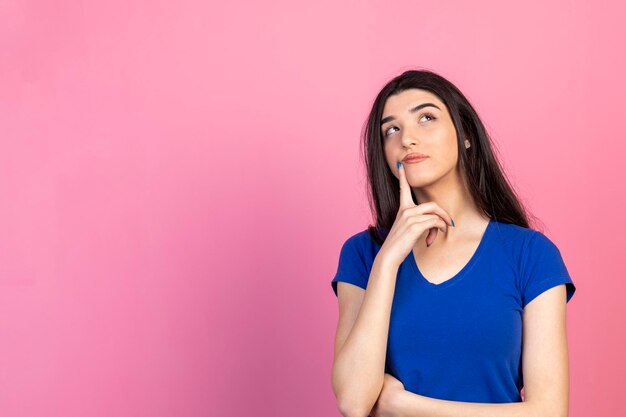 La giovane signora premurosa sta su sfondo rosa e pensa Foto di alta qualità