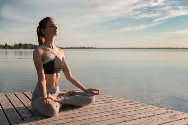 La giovane signora sportiva in spiaggia fa esercizi di meditazione.