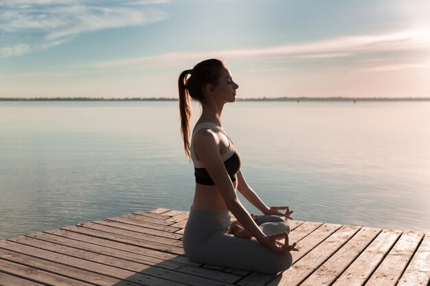 La giovane signora sportiva in spiaggia fa esercizi di meditazione.