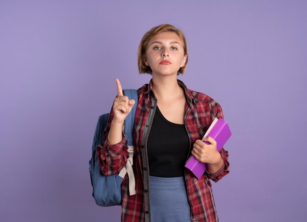 La giovane studentessa slava fiduciosa che indossa lo zaino tiene il libro e il taccuino puntati verso l'alto