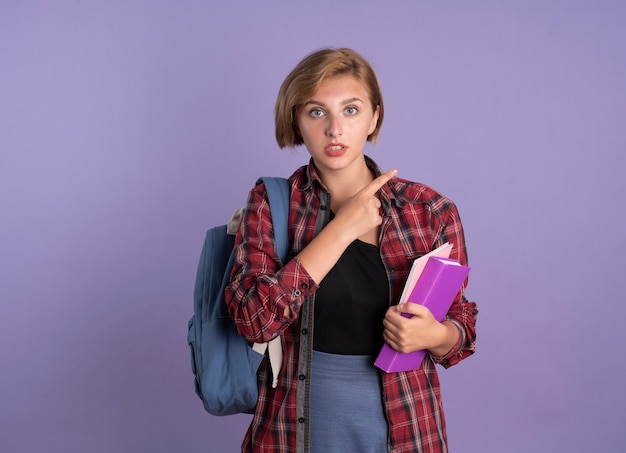 La giovane studentessa slava impressionata che indossa lo zaino tiene i punti del libro e del taccuino a lato