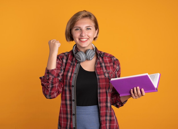 La giovane studentessa slava sorridente con le cuffie che indossa lo zaino tiene il libro in mano