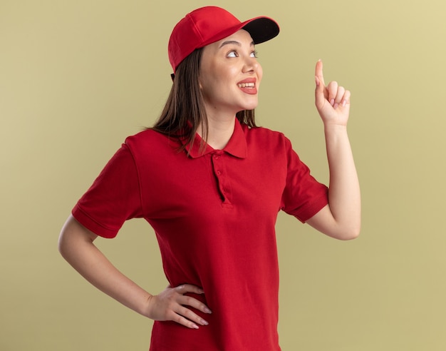 La graziosa donna delle consegne soddisfatta in uniforme guarda e punta in alto