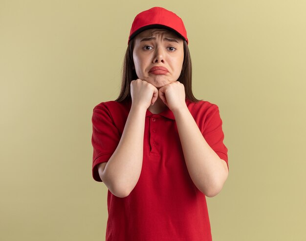 La graziosa donna delle consegne triste in uniforme mette i pugni sul mento