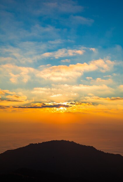 La luce del sole mattutino splende con la montagna della siluetta e il fondo nuvoloso blu.