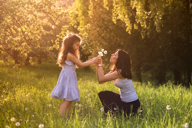 La madre e la figlia che soffiano il dente di leone fioriscono in parco