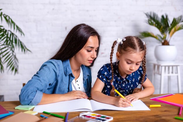 La madre e la figlia felici della famiglia disegnano insieme con i pennarelli. La donna aiuta la bambina.