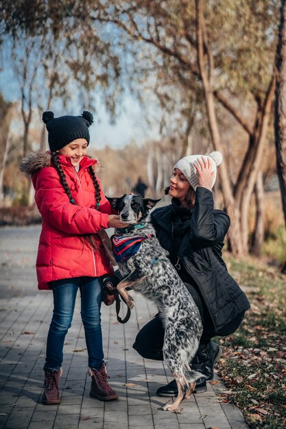 La madre felice e sua figlia camminano con il cane nel parco di autunno