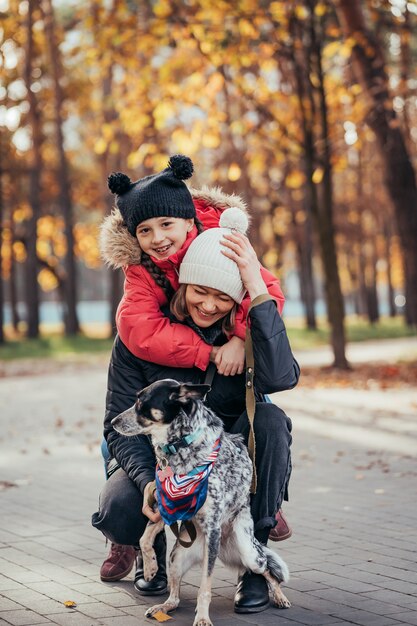 La madre felice e sua figlia che giocano con il cane in autunno parcheggiano