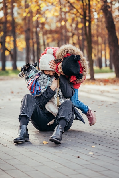 La madre felice e sua figlia che giocano con il cane in autunno parcheggiano