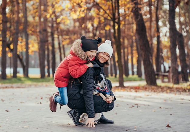 La madre felice e sua figlia che giocano con il cane in autunno parcheggiano