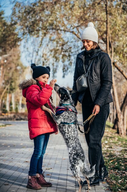 La madre felice e sua figlia che giocano con il cane in autunno parcheggiano