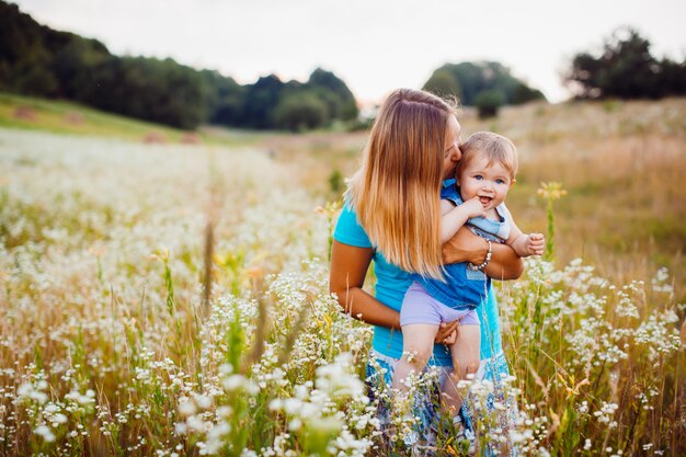 La madre si leva in piedi con un bambino sul campo con i fiori bianchi