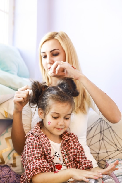 La madre sta facendo i capelli della figlia in una stanza piena di luce solare