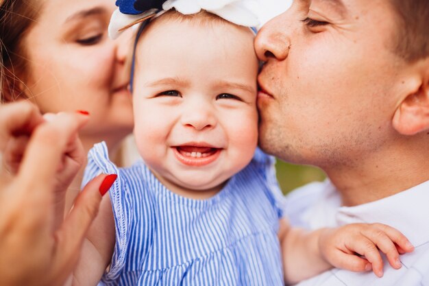 La mamma e il papà baciano la piccola ragazza sorridente tenera in vestito blu