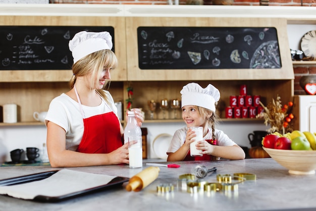 La mamma e la piccola figlia affascinante si divertono a bere latte al tavolo in una cucina accogliente