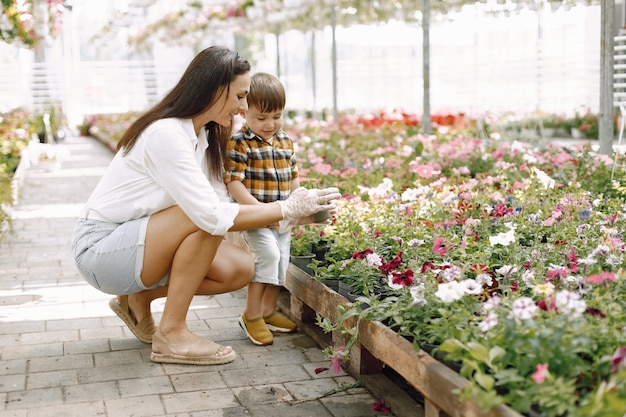 La mamma e suo figlio piantano i fiori nel vaso nella serra. Piccolo bambino che impara a piantare in una serra