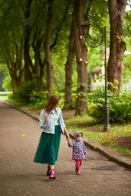 La mamma tiene la mano della figlia che cammina con lei nel parco dopo la pioggia