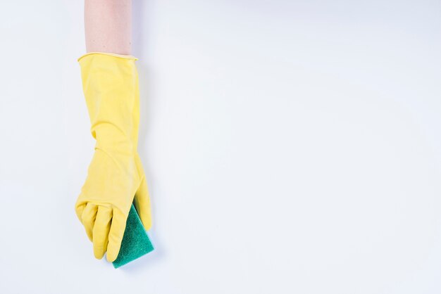 La mano del bidello con i guanti gialli che tengono spugna su fondo bianco