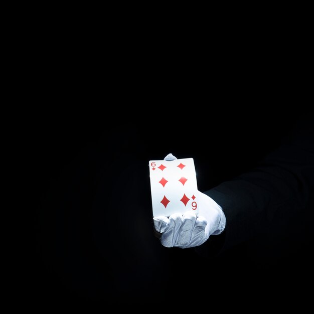 La mano del mago che mostra la carta da gioco del diamante contro fondo nero