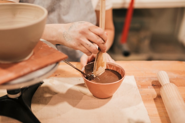 La mano del vasaio femminile che prepara la pittura per la ciotola di ceramica nell&#39;officina