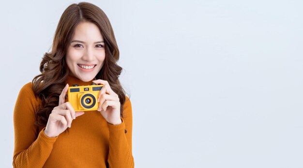 La mano del viaggiatore asiatico di bellezza della donna tiene la retro macchina fotografica gialla con il fondo bianco di sorriso felice