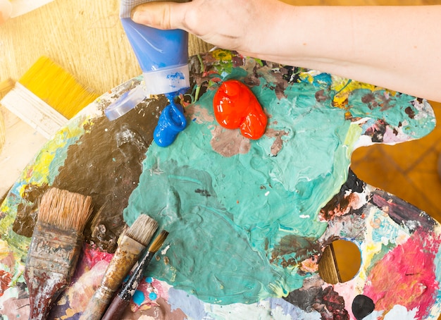 La mano dell&#39;artista che schiaccia il tubo blu della pittura ad olio sulla tavolozza sudicia