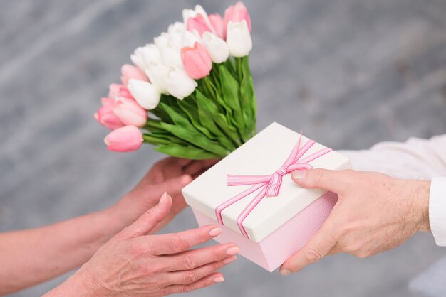 La mano dell&#39;uomo che dà il regalo di compleanno ed il mazzo dei fiori del tulipano a sua moglie