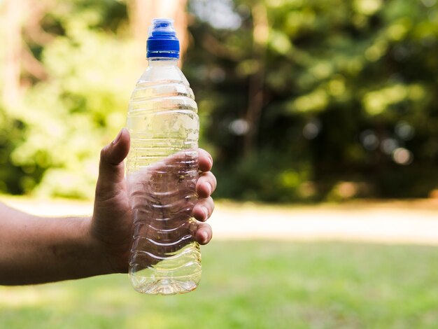 La mano dell'uomo che tiene la bottiglia di acqua di plastica vuota ad all'aperto